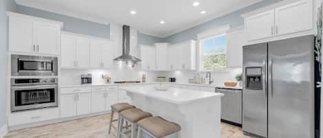 A modern kitchen with white cabinetry, stainless steel appliances, a central island with stools, and a large refrigerator.