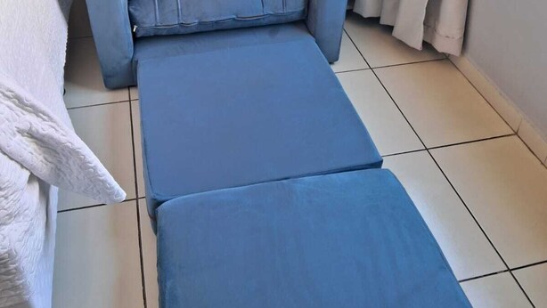 A room with a blue sofa, a white bed, and a window with curtains. - Located across from Cabo Branco Beach - Apartment with ocean view. (João Pessoa)