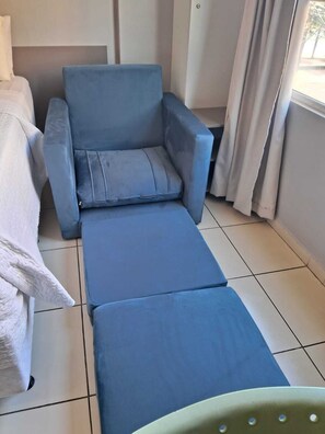 A room with a blue sofa, a white bed, and a window with curtains. - Located across from Cabo Branco Beach - Apartment with ocean view. (João Pessoa)
