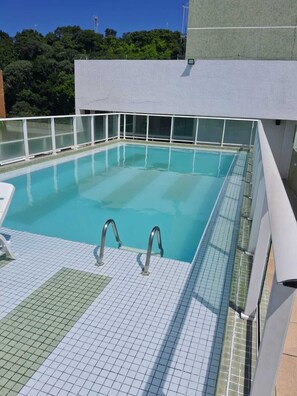 A rooftop swimming pool with clear blue water, surrounded by a white tiled deck and glass railings. - Located across from Cabo Branco Beach - Apartment with ocean view. (João Pessoa)