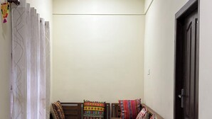 Una habitación con ventilador de techo, sofá con cojines estampados, una puerta y suelo de baldosas.