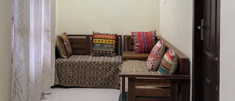 A room with a ceiling fan, a sofa with patterned cushions, a door, and a tiled floor.