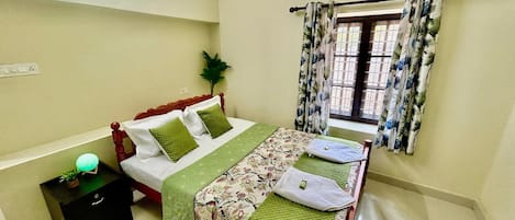 A bedroom with a bed, a nightstand, a potted plant, and a window with curtains.