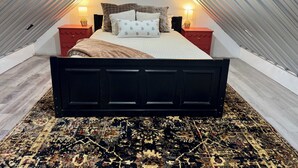 Un dormitorio con una cama, dos mesitas de noche, una alfombra y un techo inclinado.