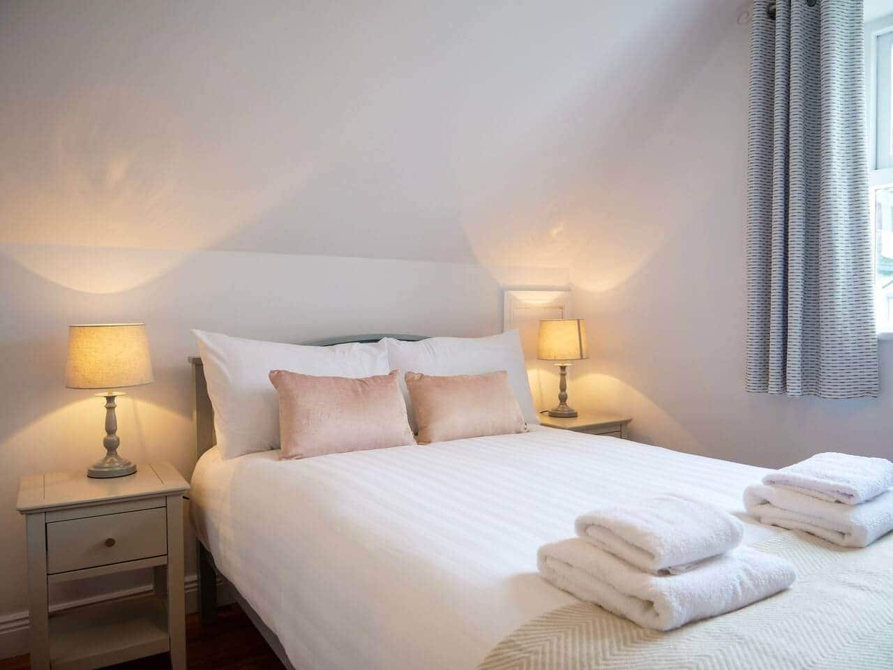 A hotel room with a neatly made bed, two bedside tables with lamps, and a window with curtains.