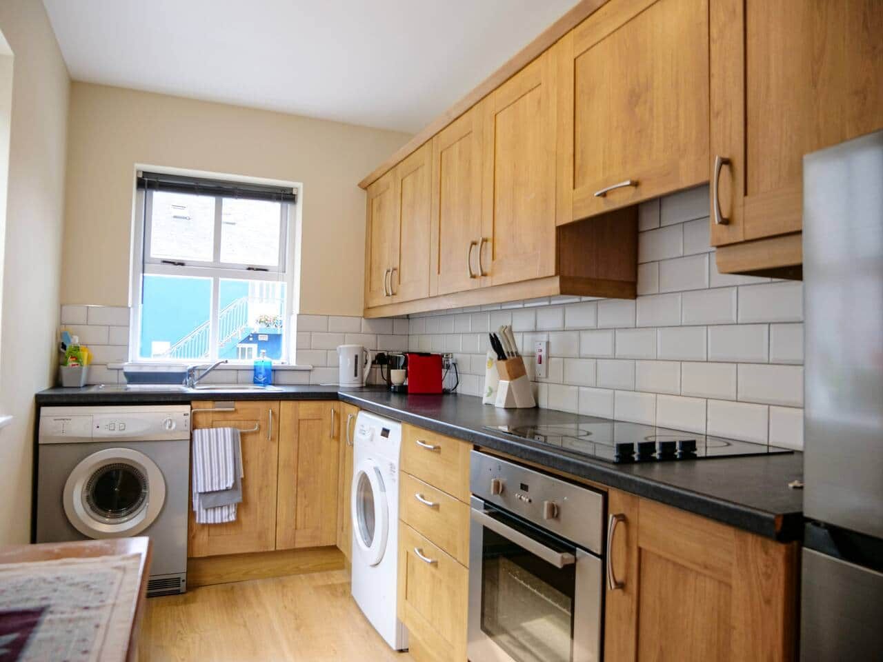 A compact kitchen with wooden cabinets, a washing machine, a stove, and a window.