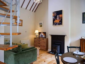 A cozy living room with a fireplace, a green sofa, a dining table with chairs, and a staircase. - Central Dingle Cottage (Dingle)
