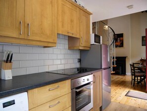 A kitchen with wooden cabinets, a black countertop, a built-in oven, and a microwave. - Central Dingle Cottage (Dingle)