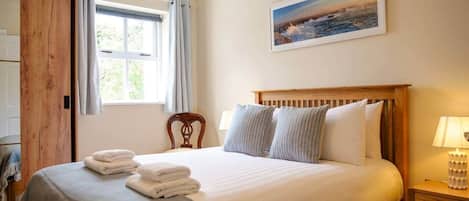 Une chambre à coucher avec un lit en bois, une table de chevet, une chaise, une fenêtre avec des rideaux et un tableau accroché au mur.