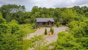 Une maison entourée d’une végétation luxuriante, avec une allée de gravier menant à l’entrée.
