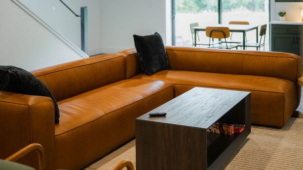 Un salon moderne avec un canapé en cuir, une table basse en bois et une vue sur l’espace repas grâce à de grandes fenêtres.