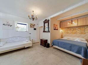A bedroom with two beds, a chandelier, a stone wall, and a window. - Natur Olive House Ston (Ston)