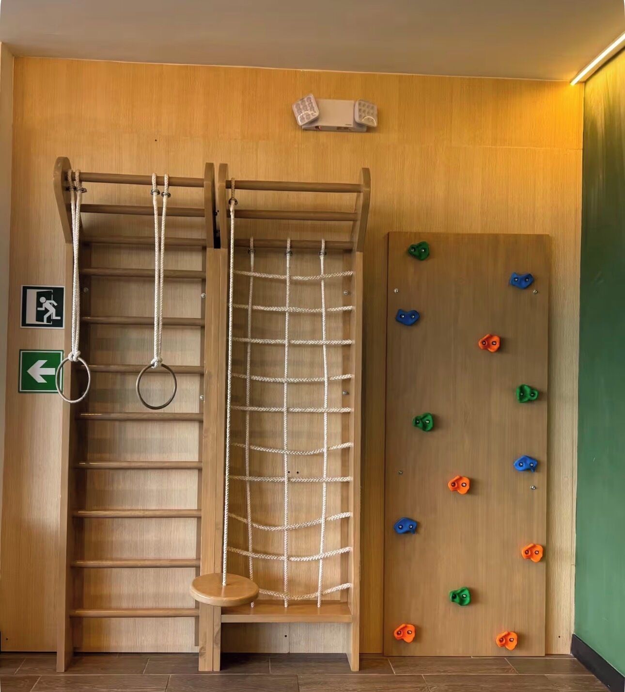 A climbing wall with various holds, a rope ladder, and a small wooden shelf.