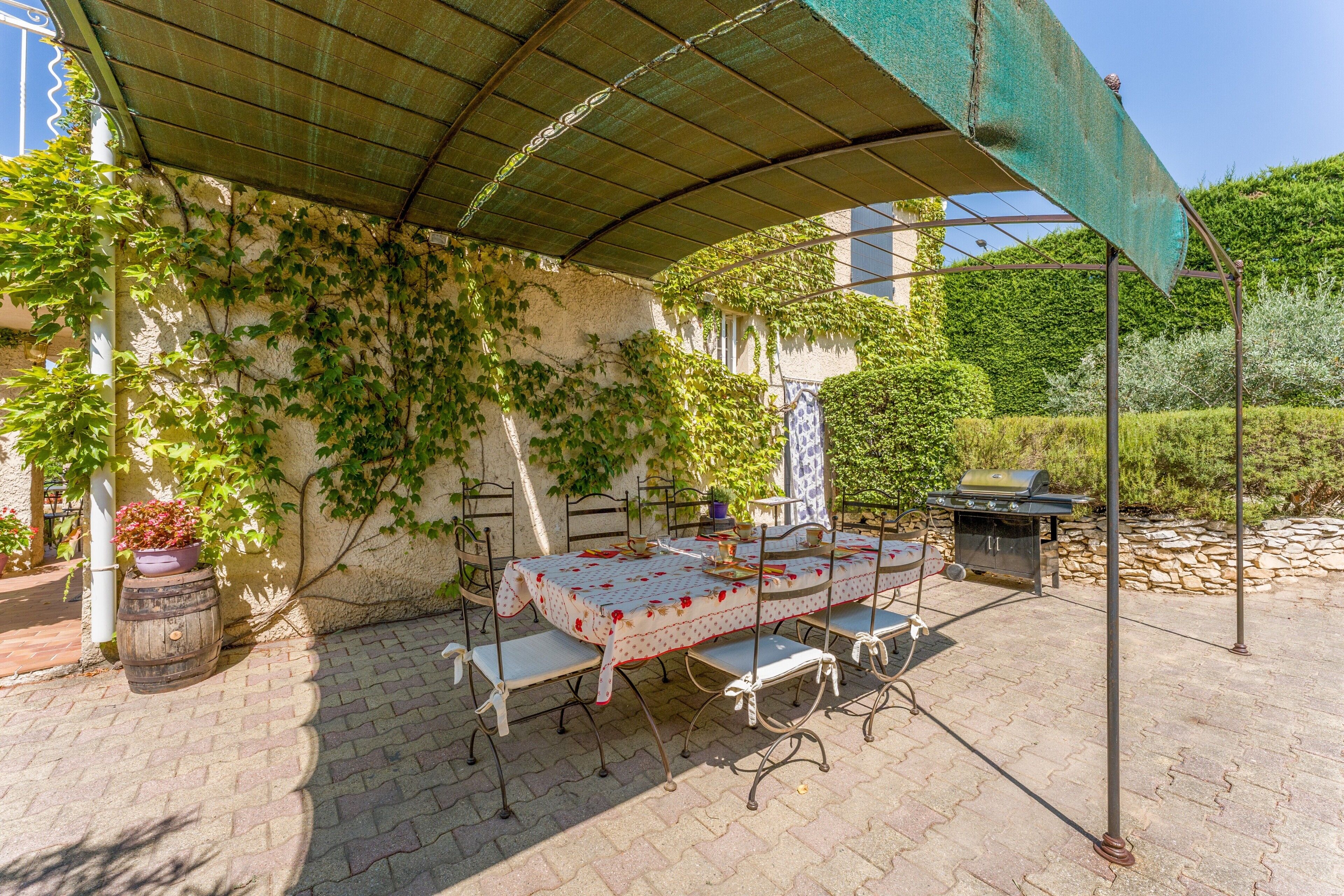 An outdoor patio with a table set for dining, a barbecue grill, and a covered area with a metal roof.