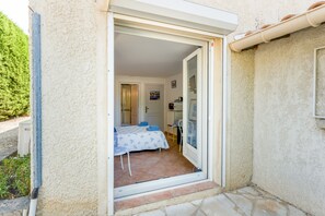 A room with a bed, a table, and a chair, a door leading to another room, and a small balcony area.
