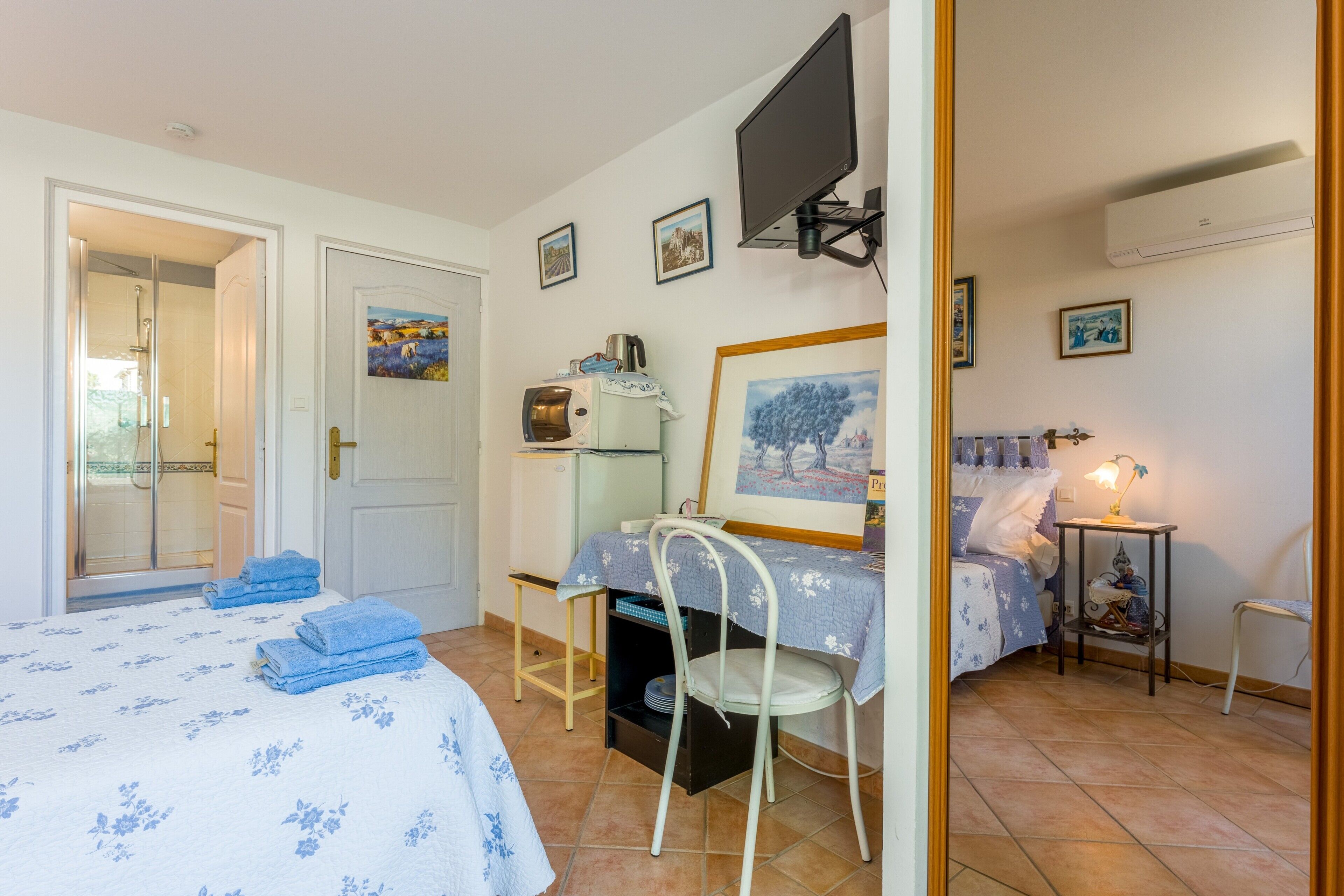 Quarto com cama, poltrona, mesa, televisão e chuveiro.