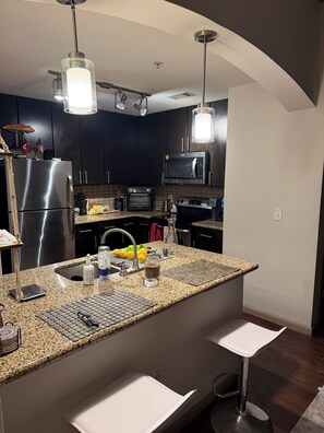 A modern kitchen with dark cabinetry, stainless steel appliances, a granite countertop, and pendant lighting. - Perfect Family location for a Houston visit (Houston)
