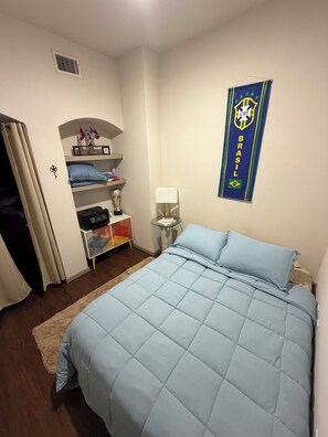 A bedroom with a bed, a nightstand, a lamp, a shelf with flags, and a wall hanging. - Perfect Family location for a Houston visit (Houston)