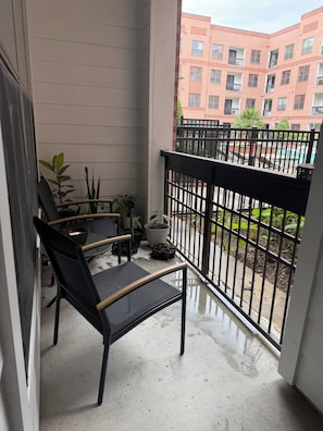 A balcony with a black chair, potted plants, and a view of a red brick building. - Perfect Family location for a Houston visit (Houston)