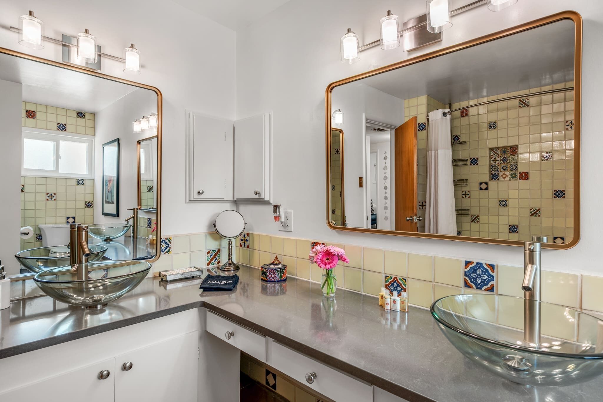 A modern bathroom with two glass sinks, a large mirror, and a vanity with drawers.