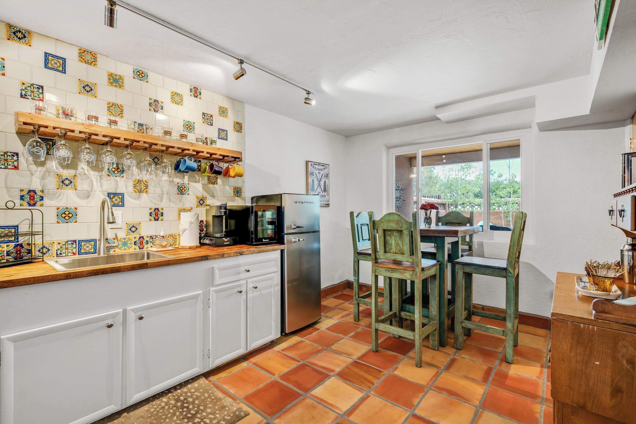 A kitchen with white cabinets, a tiled backsplash, a refrigerator, and a dining area with a table and chairs.