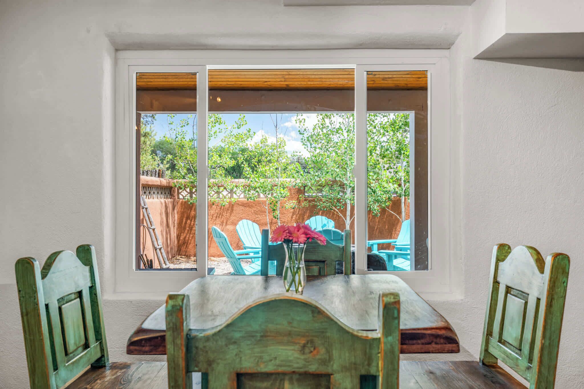 A dining area with a table and chairs, a window with a view of a backyard, and a vase with flowers on the table.