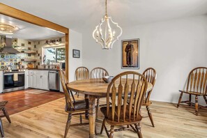 A dining area with a wooden table and chairs, a chandelier, and a kitchen in the background. - Family-friendly Adobe, Walk Everywhere (Santa Fe)