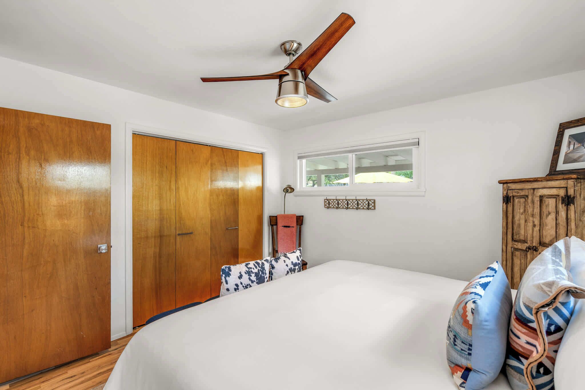 A bedroom with a bed, a ceiling fan, a window, a wardrobe, and a bedside lamp.