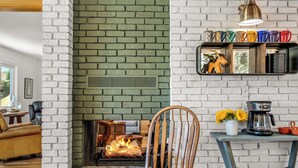 Een woonkamer met een haard van baksteen, een houten stoel, een bijzettafeltje en een plank met mokken en een decoratief object.