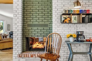 A living room with a brick fireplace, a wooden chair, a coffee table, and a shelf with mugs and a decorative item. - Family-friendly Adobe, Walk Everywhere (Santa Fe)
