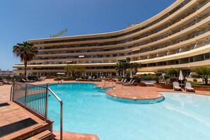 Ein Hotel mit großzügiger Poolanlage, mehreren Balkonen und blauem Himmel.