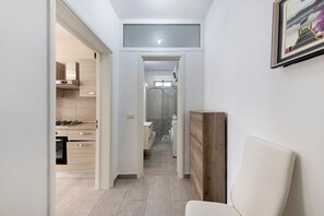 En smal hall med ett kök på ena sidan och en tvättstuga på den andra, inredd i en modern stil med ljusfärgade kakelplattor och träinredning.
