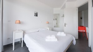 Habitación de hotel con una cama grande, dos mesitas de noche con lámparas, un espejo y una silla roja.