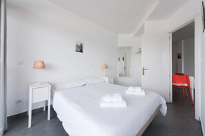 Ein Hotelzimmer mit einem großen Bett, zwei Nachttischen mit Lampen, einem Spiegel und einem roten Sessel.