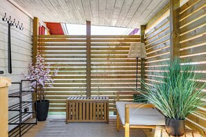 Ein Zimmer aus Holz mit einer Bank, einem Tisch, einer Hängeleuchte, einem Topfpflanze und einem Hakenstange.