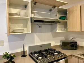 A kitchen with a gas stove, microwave, and open shelving with dishes and a green basket. - Relaxing 3BR Escape  Private Jacuzzi & BBQ (Punta Cana)