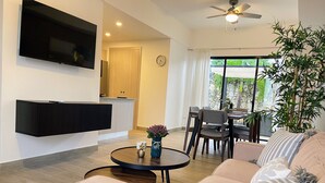 Ein modernes Wohnzimmer mit Flachbildfernseher, einer Sofagarnitur, einem Esstisch und einem Deckenventilator.