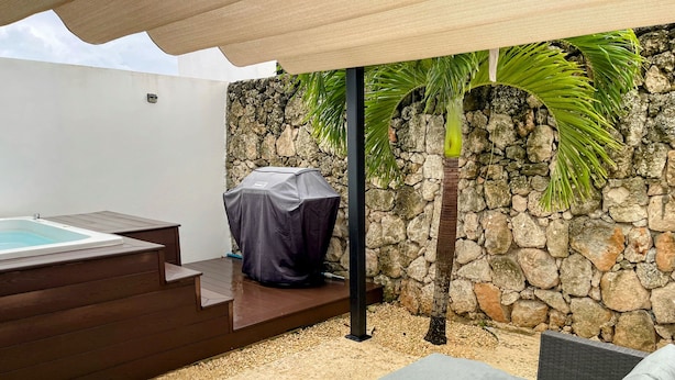 Eine moderne Außenpatio mit Whirlpool, einer überdachten Grillstation und einer Steinwand.