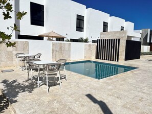 A modern outdoor pool area with a white building, a table with chairs, and a black fence. - Relaxing 3BR Escape  Private Jacuzzi & BBQ (Punta Cana)