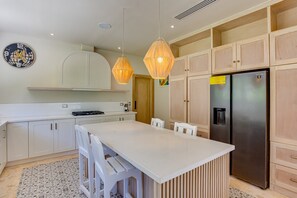 Eine moderne Küche mit Kochinsel, Holzschränken, einem Edelstahlkühlschrank und Pendelleuchten.