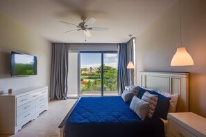 A bedroom with a bed, a TV, a dresser, a ceiling fan, and a view of a garden through a sliding door. - Luxury 8BR Villa Hacienda  Punta Cana (Punta Cana)