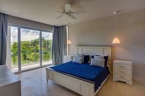 Ein Schlafzimmer mit einem großen Bett, zwei Nachttischen, einem Deckenventilator und Blick auf Grünflächen.