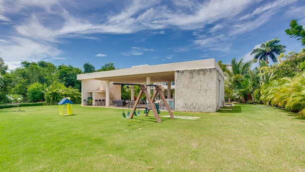 A modern house with a covered patio, a swing set, and a well-maintained lawn. - Luxury 8BR Villa Hacienda  Punta Cana (Punta Cana)