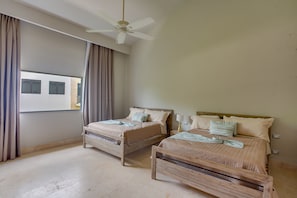 Un dormitorio con dos camas de madera, un ventilador de techo y una ventana con cortinas.