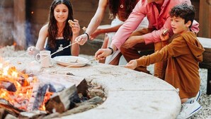 Eine Familie versammelt sich um ein Lagerfeuer mit Grill und röstet Marshmallows.