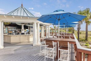 A covered outdoor seating area with wooden tables and chairs, a bar with a sign reading 'SAI SALTY', and palm trees in the background. - 2 Bedroom Villa Beach Access at SurfWatch Resort (Hilton Head Island)
