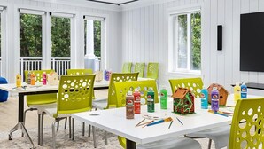 Ein Zimmer mit einem weißen Tisch, grünen Stühlen und verschiedenen Kunstmaterialien.