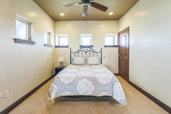 A bedroom with a bed, a ceiling fan, and a door.