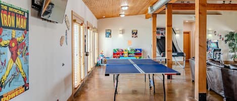 A room with a ping pong table, wooden ceiling, and various posters on the walls.