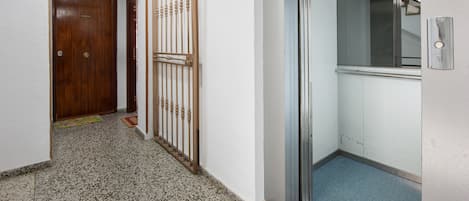 Un couloir avec une porte en bois, un portail en métal et un ascenseur.